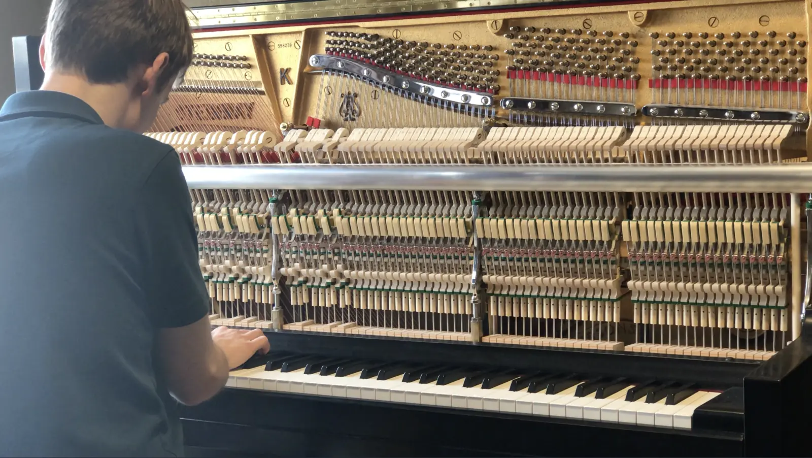 Sean practicing at an open upright piano in daylight